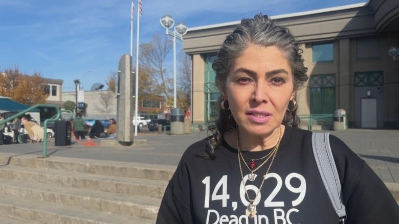 A woman stands outside. Her shirt reads 14,629 dead in B.C.