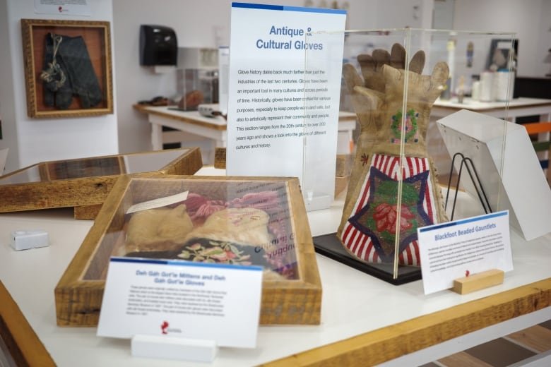 A collection of gloves enclosed in glass boxes on a table. Next to each glove there is a card with description about them.