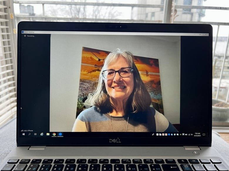 A middle-aged white woman sitting in front of a painting is seen on a laptop screen during a Zoom call.