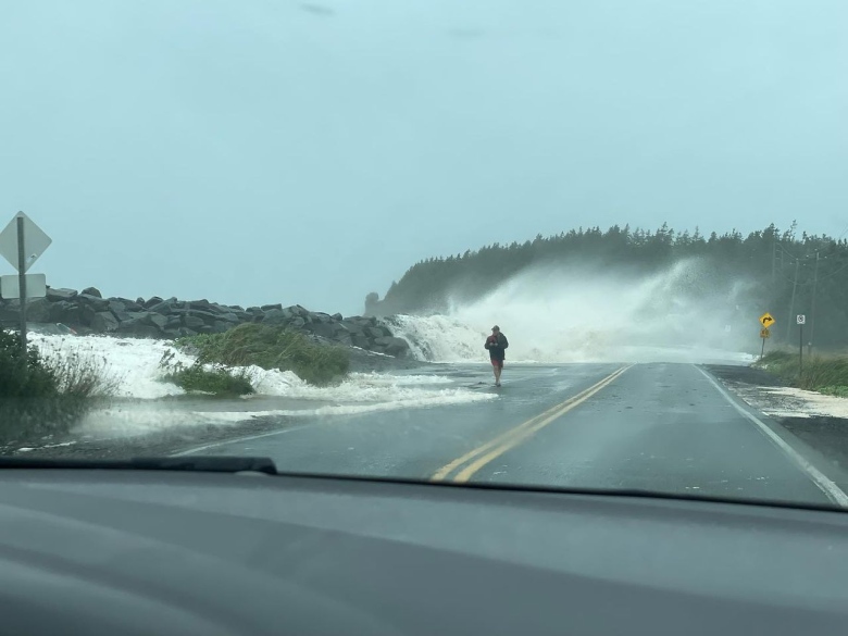 Ocean water crashes over a rock wall onto a road.