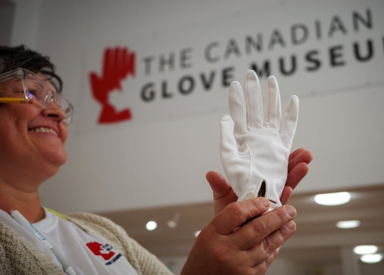 A woman cradles a formal white glove in her hands. Behind her is a sign for the Canadian Glove Museum.