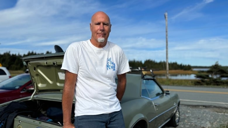 A man leans against the trunk of a vintage car.