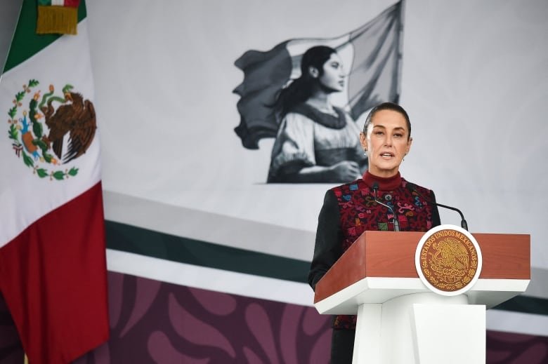 A woman speaks at a podium. The Mexican flag is behind her.