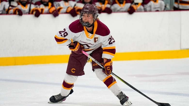 A women's hockey player in a white jersey takes a wrist shot.