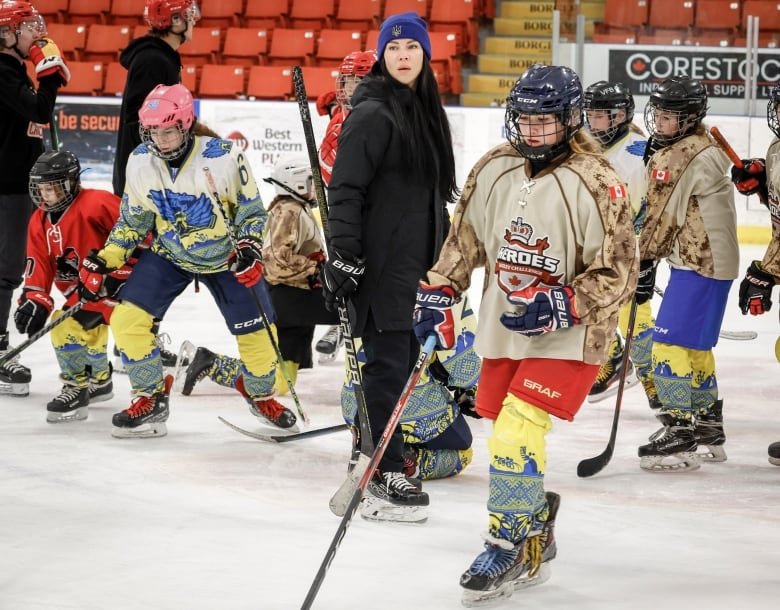 half a dozen hockey player youths on the ice, with an older female coach in a black coat.