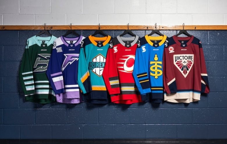 Six hockey jerseys are hung on the wall of a hockey dressing room.