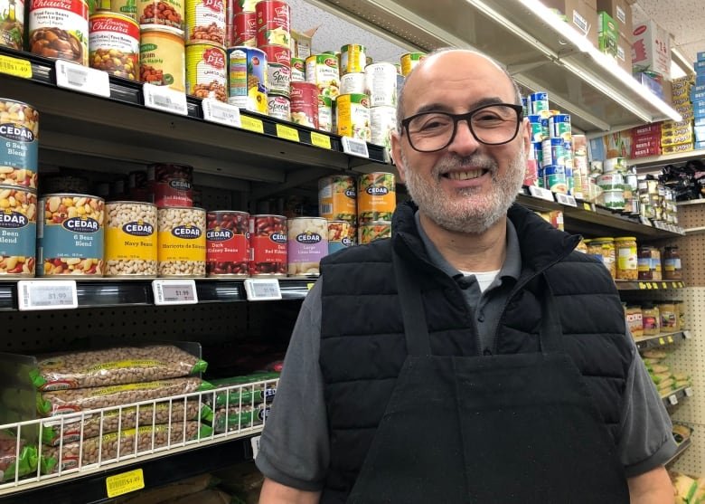 A man stands in a food aisle, smiling at the camera.