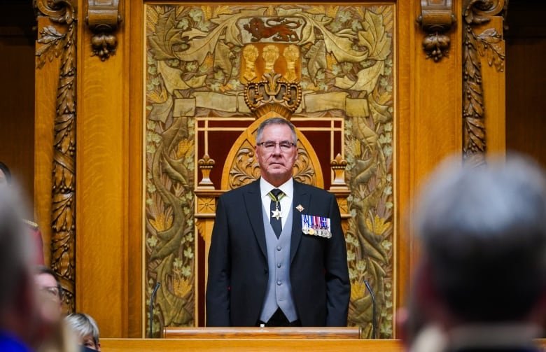 A man in a three piece suit stands at attention in the Saskatchewan legislature.