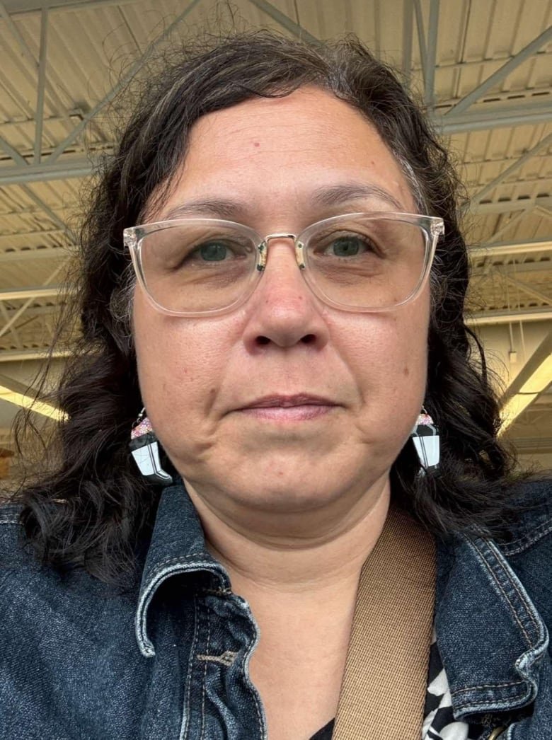 A woman in a close-up headshot wearing glasses and dangling earrings.