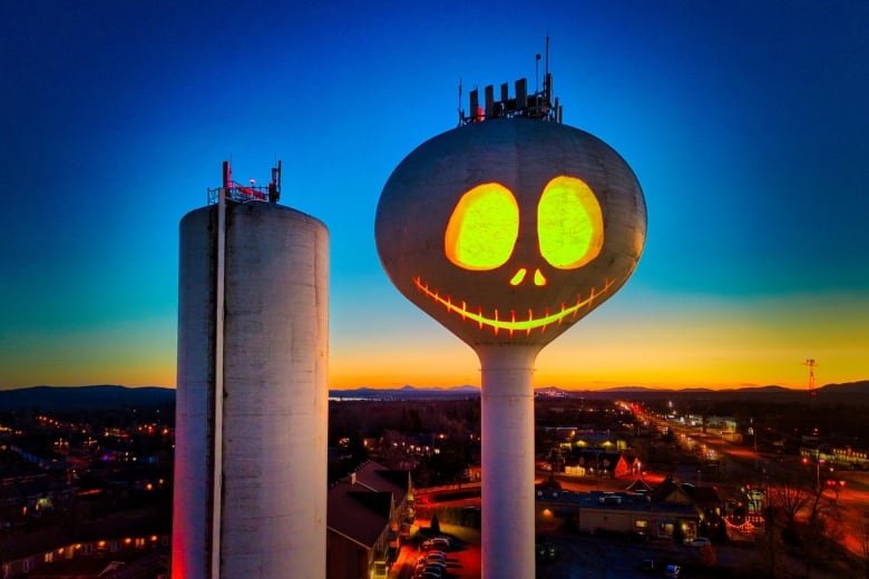 A projection on a watertower displays a smiling pumpkin