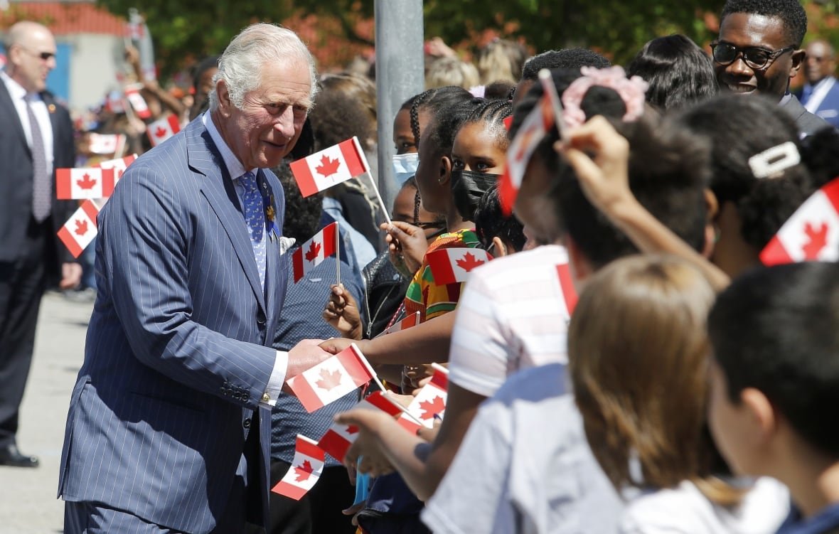 An adult shakes hands with children. Many of them are holding small Canadian flags.