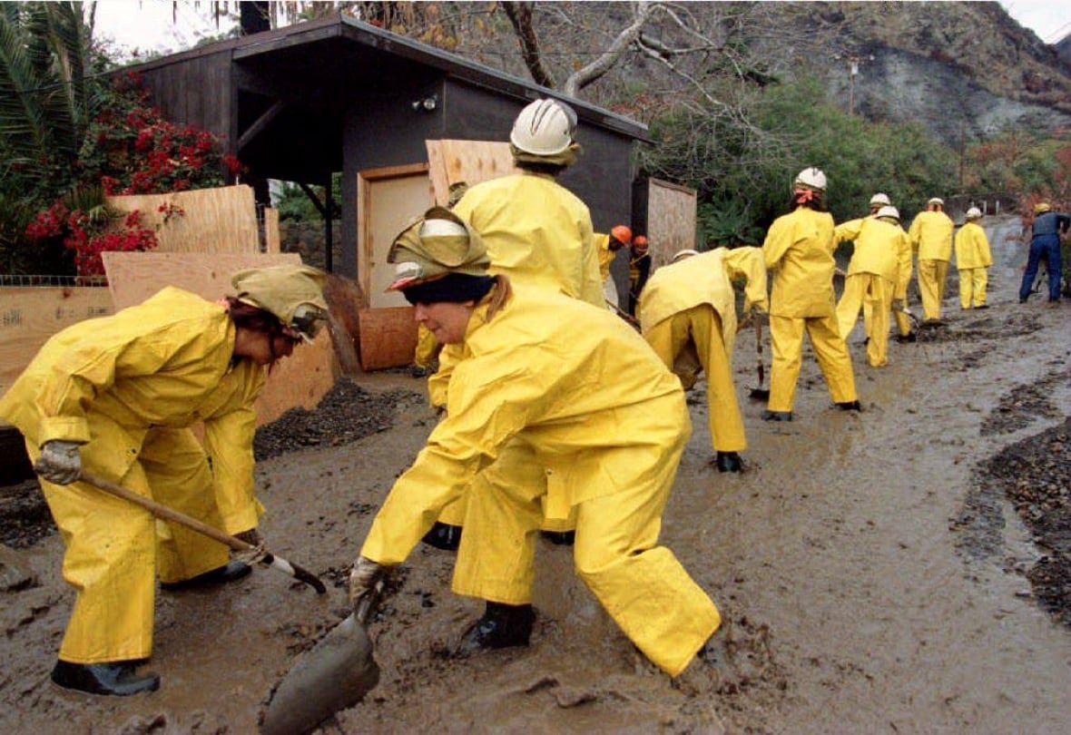 A group of workers in yellow rainjackets shovel mud