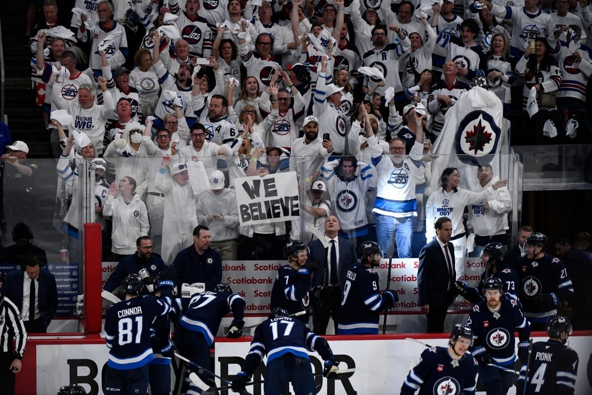 hkn-blues-jets-20250504-1 Group of fans wearing white and blue jerseys cheer, while one holds a sign that says "we believe" in all caps