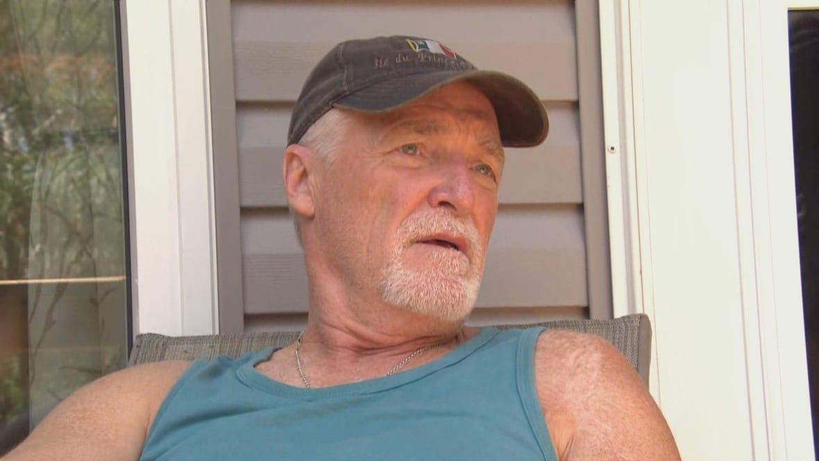 alain-landry-resident-in-sandy-bay-cottage-area-of-victoria-beach-rm A man with a black hat, white goatee and turquoise muscle shirt looks off in the distance.
