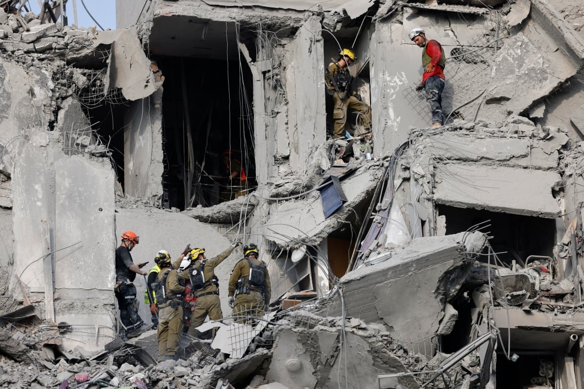 2221137457 Helmeted rescue workers can be seen navigating a heavily damaged building, with concrete debris all around.