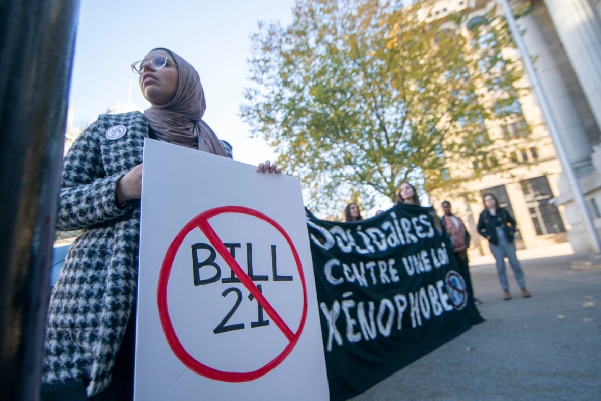 bill-21-protesters-outside-quebec-court-of-appeal A woman in a hijab holds a sign with Bill 21 crossed out. Others hold a black banner.
