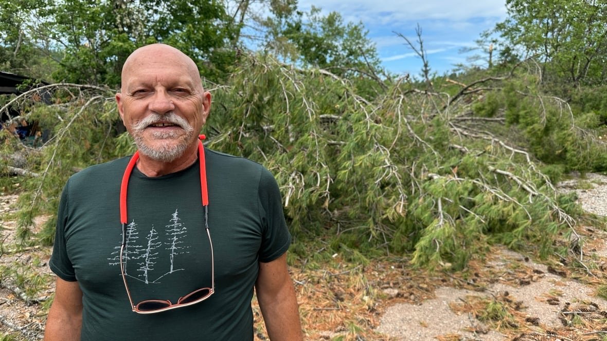 bill-steer A man wearing a green T-shirt standing in front of a fallen tree.