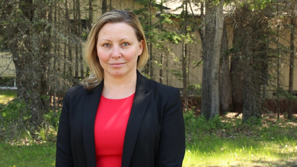 heather-exner-pirot A woman in a red dress and black blazer poses for a picture in a park on a sunny day.