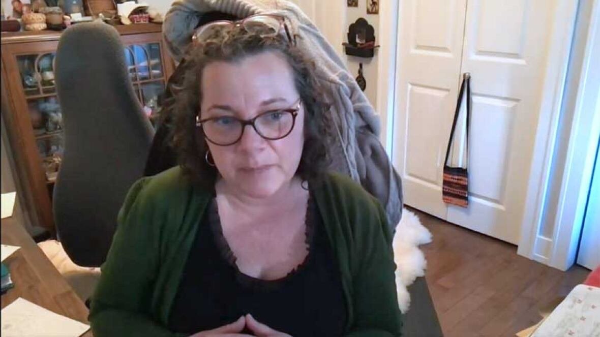 lori-ann-roness-patient-advocate-sackville A woman with dark, wavy, shoulder-length hair, wearing glasses, a black top and green cardigan, sitting in a home office.