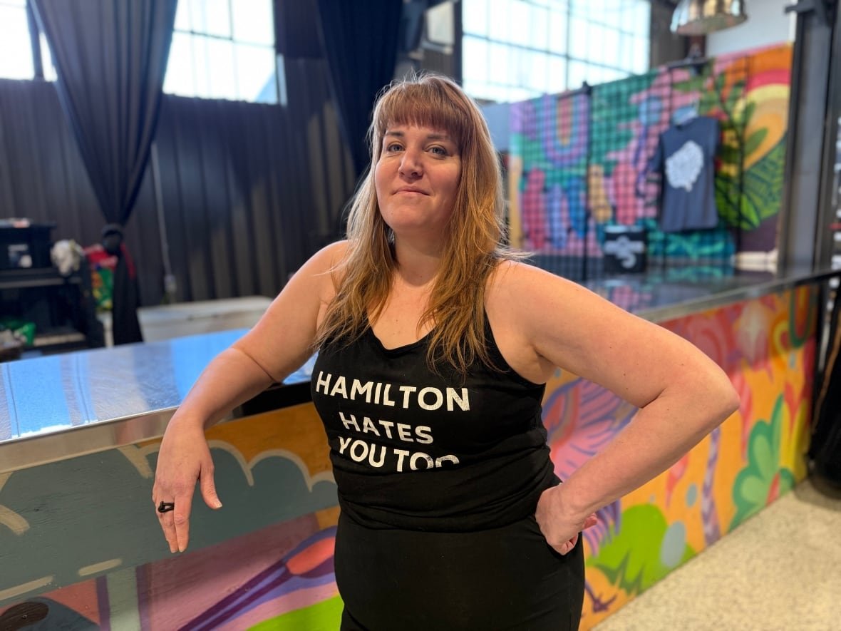 max-goodis Woman stands at colourful bar with a shirt that says "Hamilton hates you too"