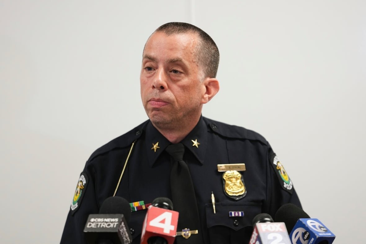 michigan-church-shooting-1 Man in a police uniform stands in front of microphones at a podium.