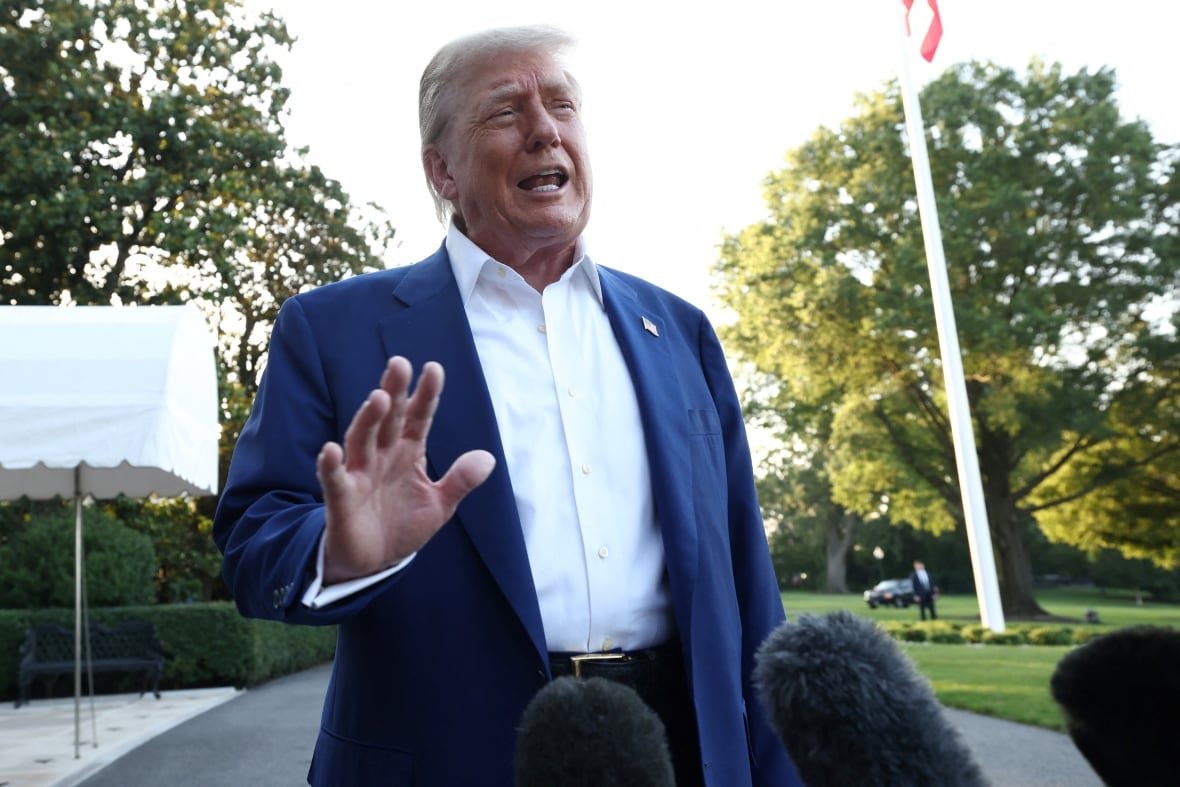 nato-summit-trump A man in a white shirt and blue jacket speaks into microphones.