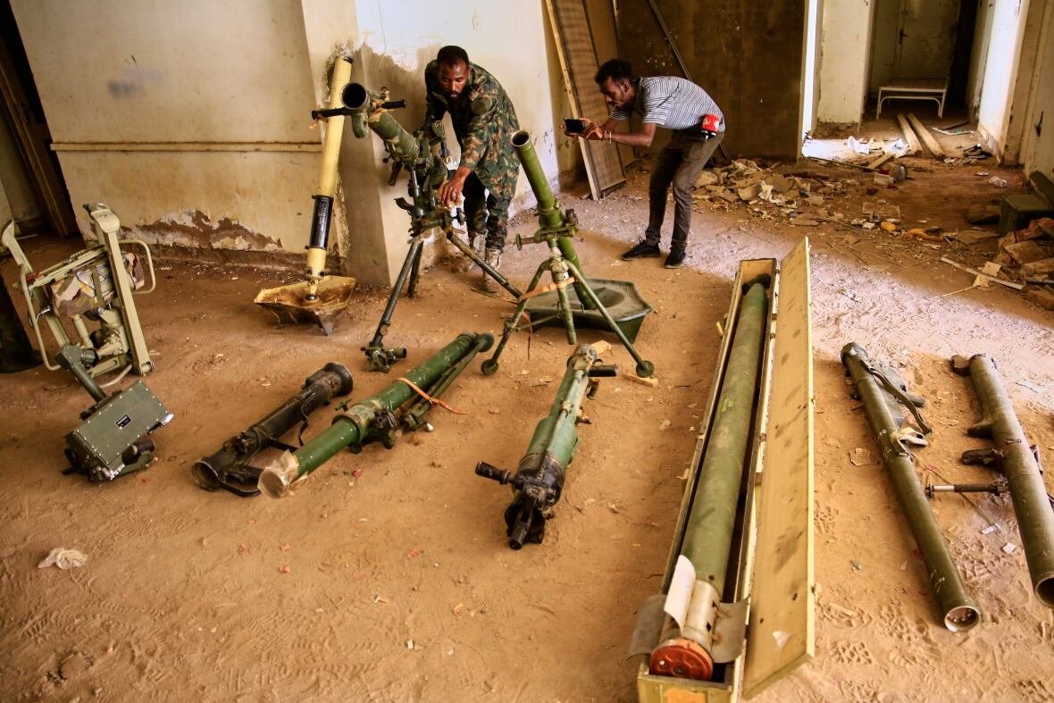 sudan Two men are shown with a cache of weapons laid on dirt ground.