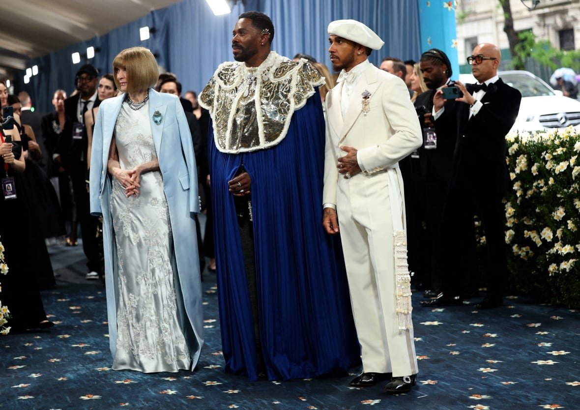 usa-met-ball-2 Three people stand together with a crowd of other people visible past them. A woman wears a silver dress and a powder blue coat, next to a man in a blue overcoat/cape situation with embellishment around the neck and shoulders, and on the far right stands a man in an ivory suit.