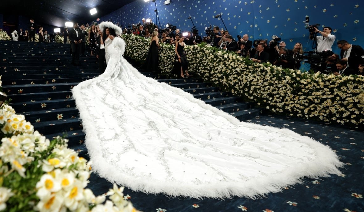 usa-met-ball-3 A woman stands on a staircase with a massive white train spread out down the steps behind her.