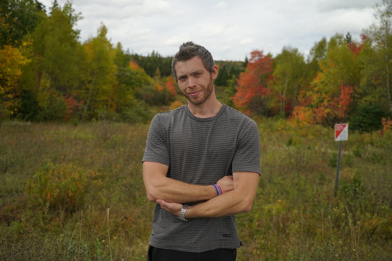 Man in grey t-shirt stands near trees