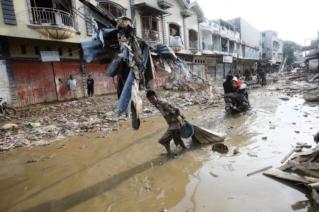 A boy drags a sack through a road flooded with muddy water.