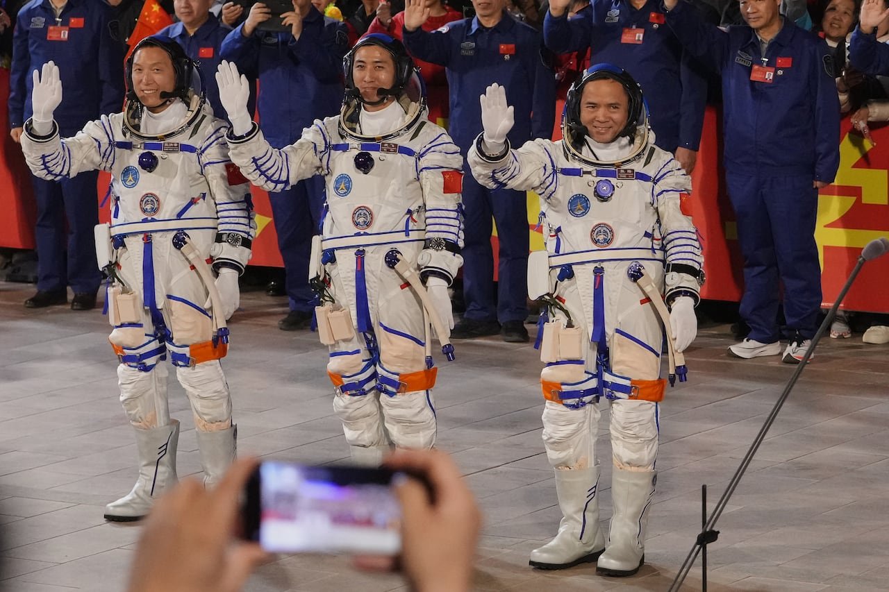 Three Chinese astronauts wave in full space suits.
