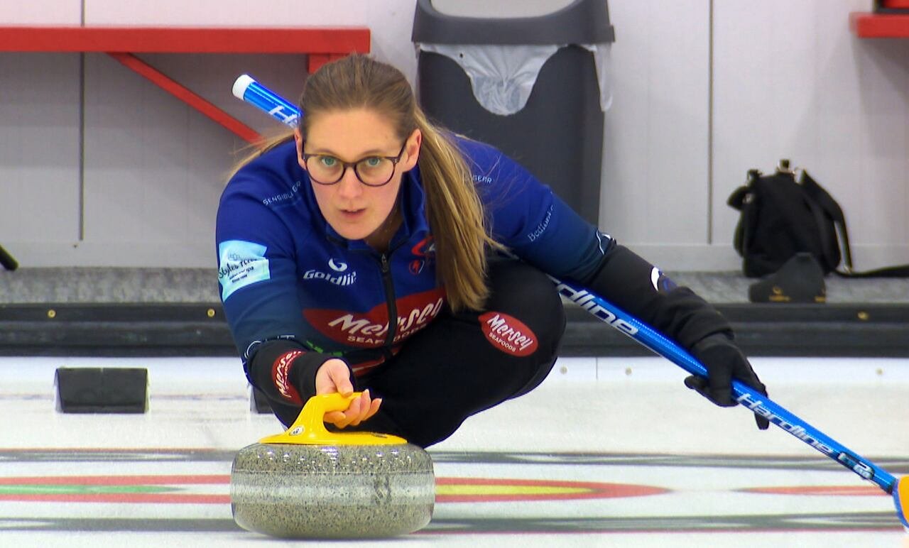 A curler wearing glasses and a ponytail is shown sliding down the ice.