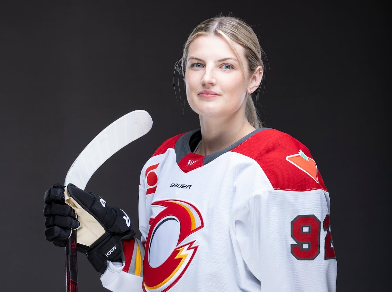 default-57 A women's hockey player wearing a jersey with a white base, with red shoulder patches, yellow, red, and light grey striping and the team's "O" logo prominently displayed on the front.