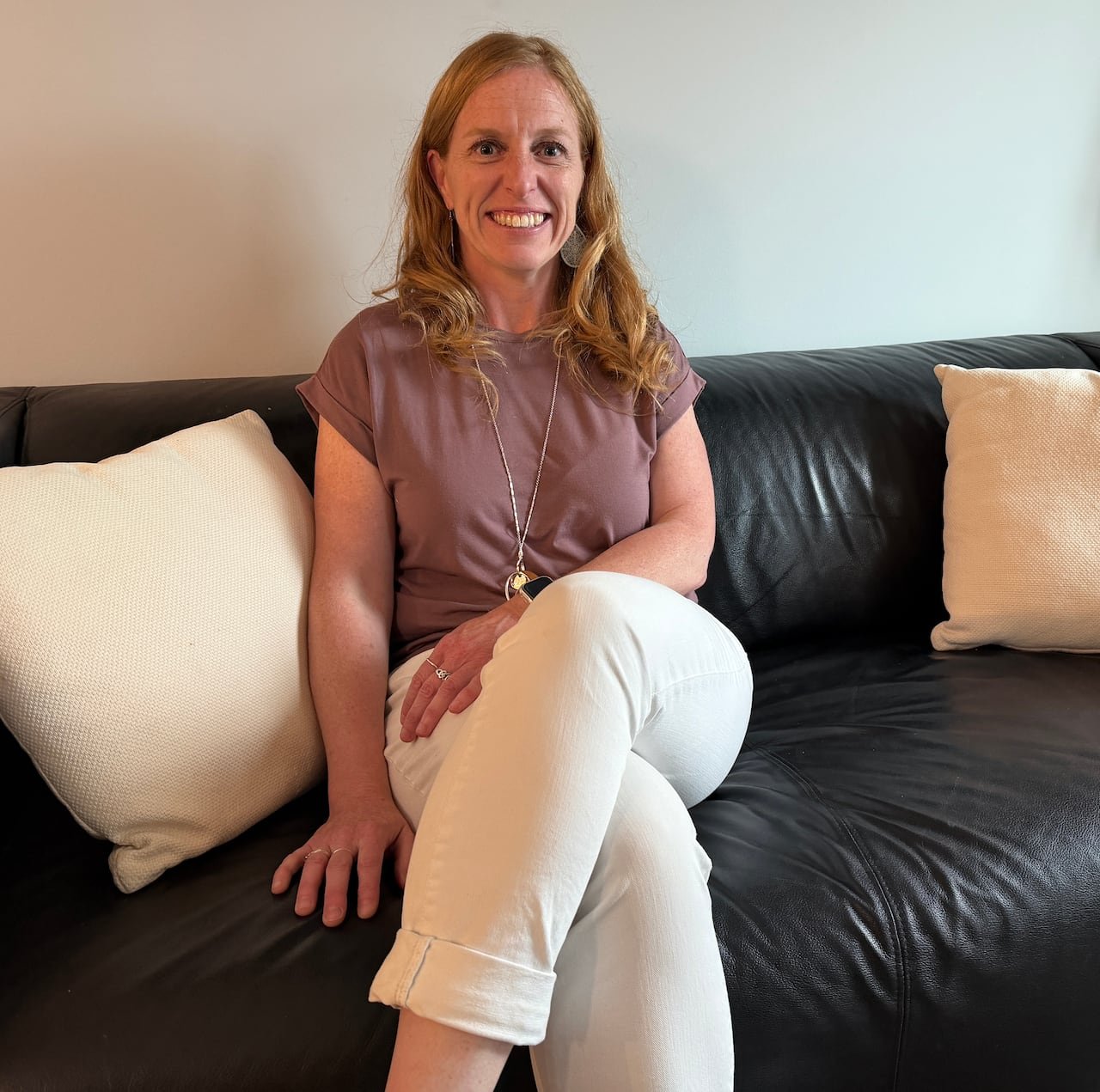 default-693 Woman smiling sitting on a sofa wearing white jeans and a mauve t-shirt.