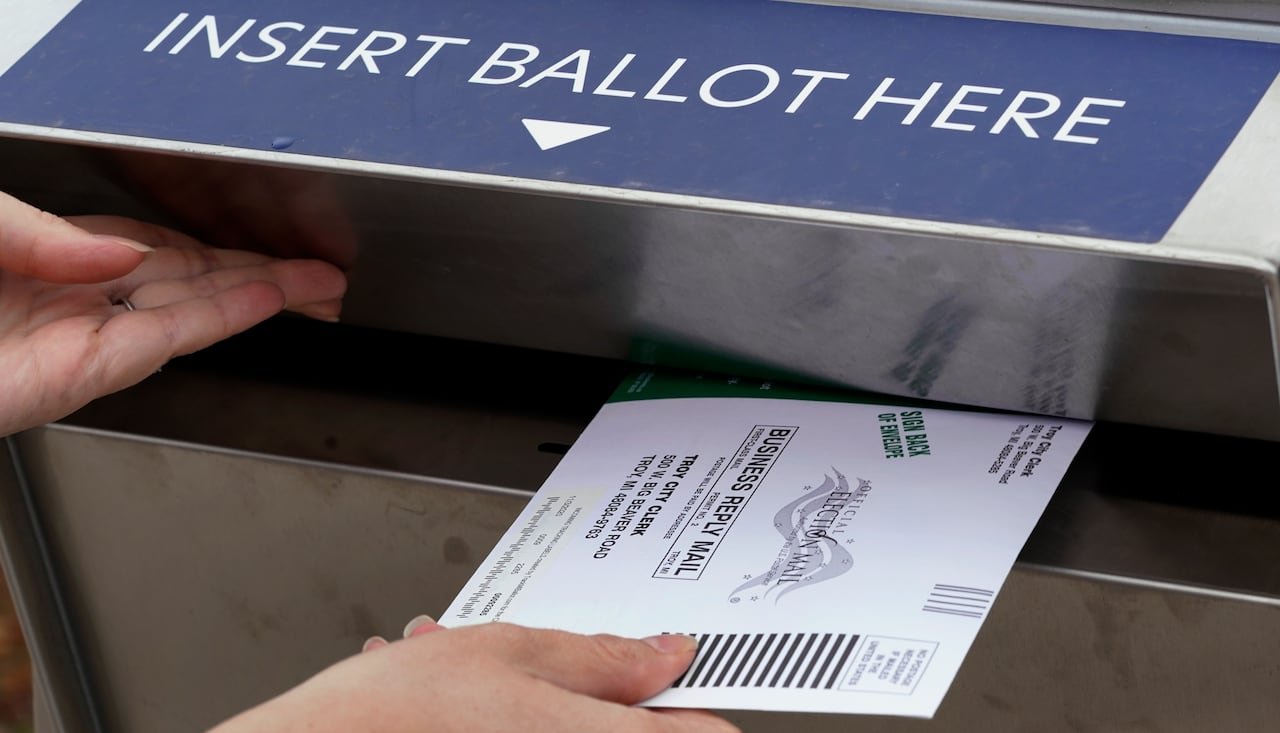 default-769 A hand holds a mail-in ballot envelope at the opening of a drop box labelled 'Insert Ballot Here'