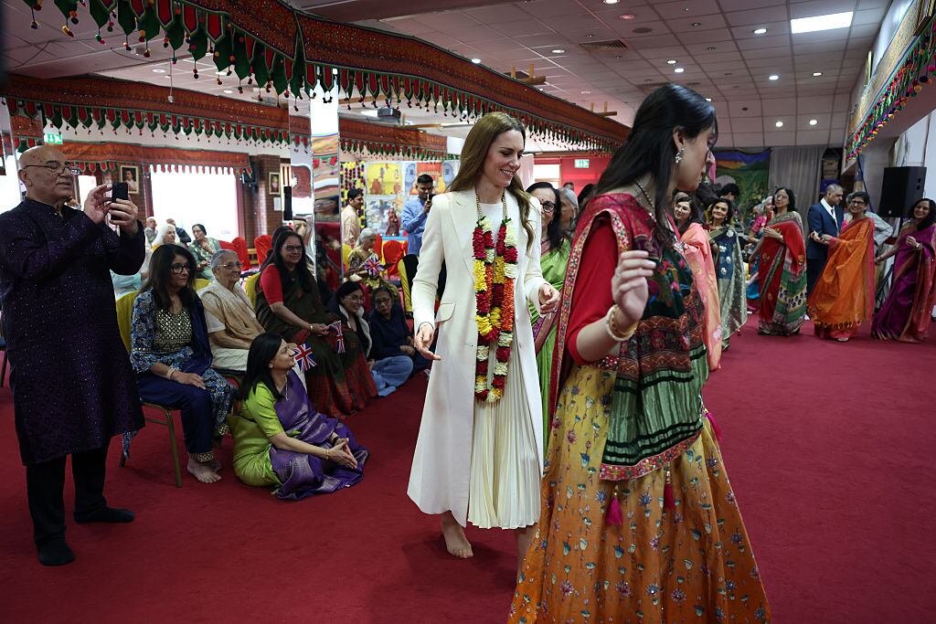 A person participates in a traditional dance during a royal visit.